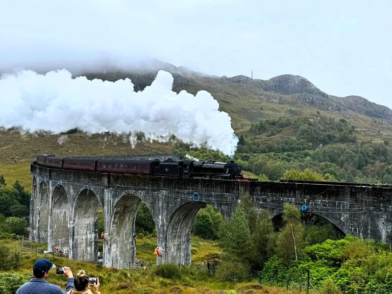Coach travelers photographing the Glenfinnan Viaduct and Glencoe mountains on a Glenfinnan Viaduct and Glencoe tour from Edinburgh, Scotland
